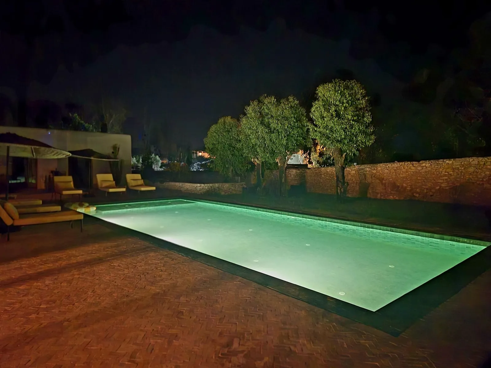 La piscine illuminée à la nuit tombée, reflets vert émeraude